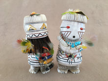 Load image into Gallery viewer, This set is a depiction of first man and woman. There is a lot going on in this set. The man wears a parrot feather Head pin with his eyes inlaid with gold lip mother of pearl. His teeth are zigzag with pipe stone and black jet pigment. Under his teeth is has a horse hair beard. Holding in his hand on the right is a bamboo with parrot feather prayer plume. Opposite hand holding more parrot feathers and a ladder of six corn representing the sacred directions. These are made of white shell, red spiny oyster s