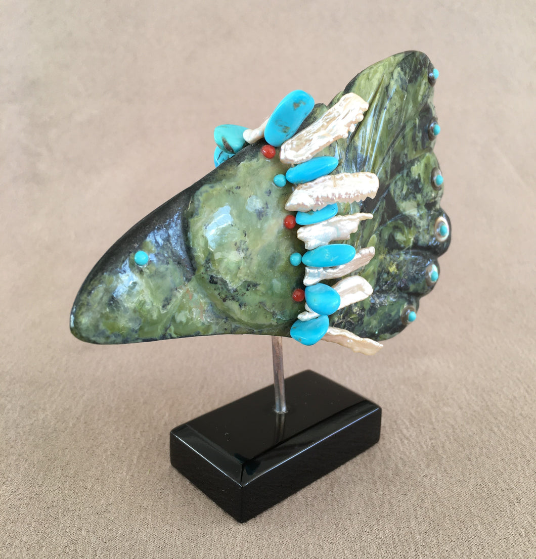 A triangle shaped green found stone carved into a bird. It is inlaid with natural sleeping beauty turquoise, coral and abalone. The offering bundle is made of kingman turquoise and baroque pearls. This bird is pinned in place with a heavy sterling silver on a black belgian marble base. 